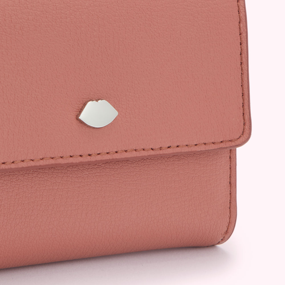 Close-up of a dusty rose pink leather wallet with a silver lip-shaped detail.
