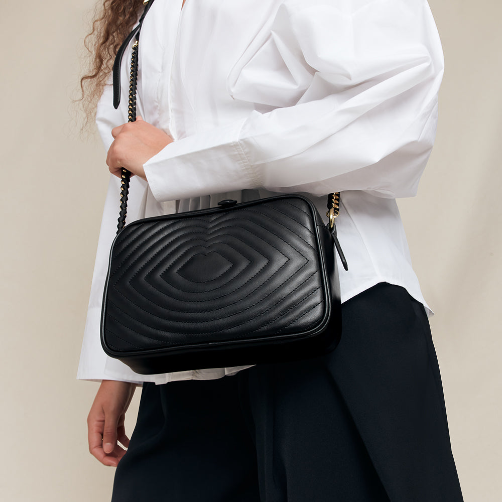 Person holding a black quilted handbag against a neutral background