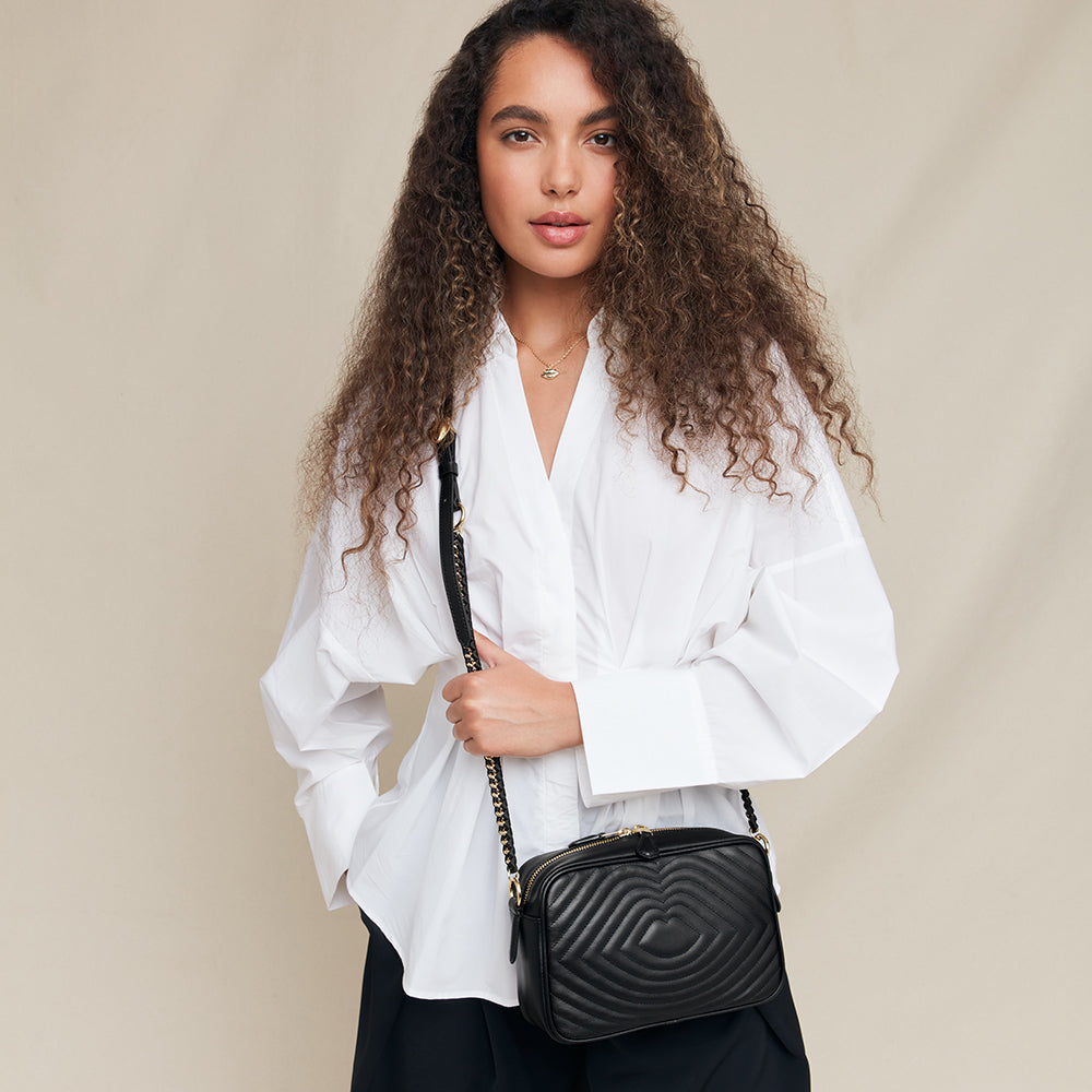 Woman holding a black quilted handbag against a beige background