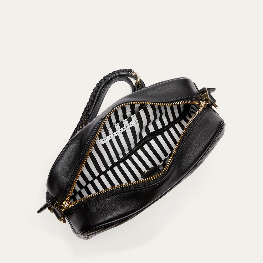 Black crossbody bag with gold zipper and striped interior on a white background