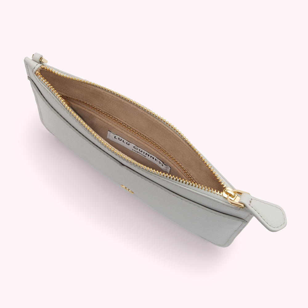 Overhead view of a light teal Lulu Guinness zip-around pouch open to reveal its beige interior and gold zipper.