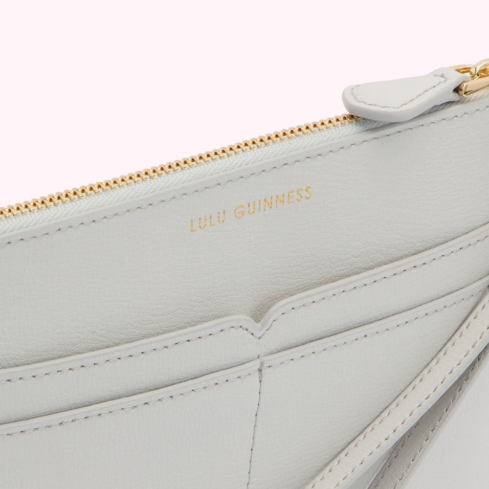 Close-up view of the inside of a light grey Lulu Guinness zip-around wallet, showing the brand name and interior compartments.
