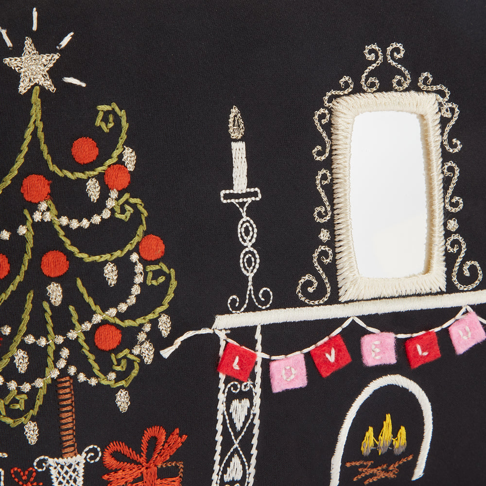 Close-up of embroidered Christmas scene on black fabric, featuring a Christmas tree, fireplace with mantle, mirror, candle, and bunting that spells "Lovely".