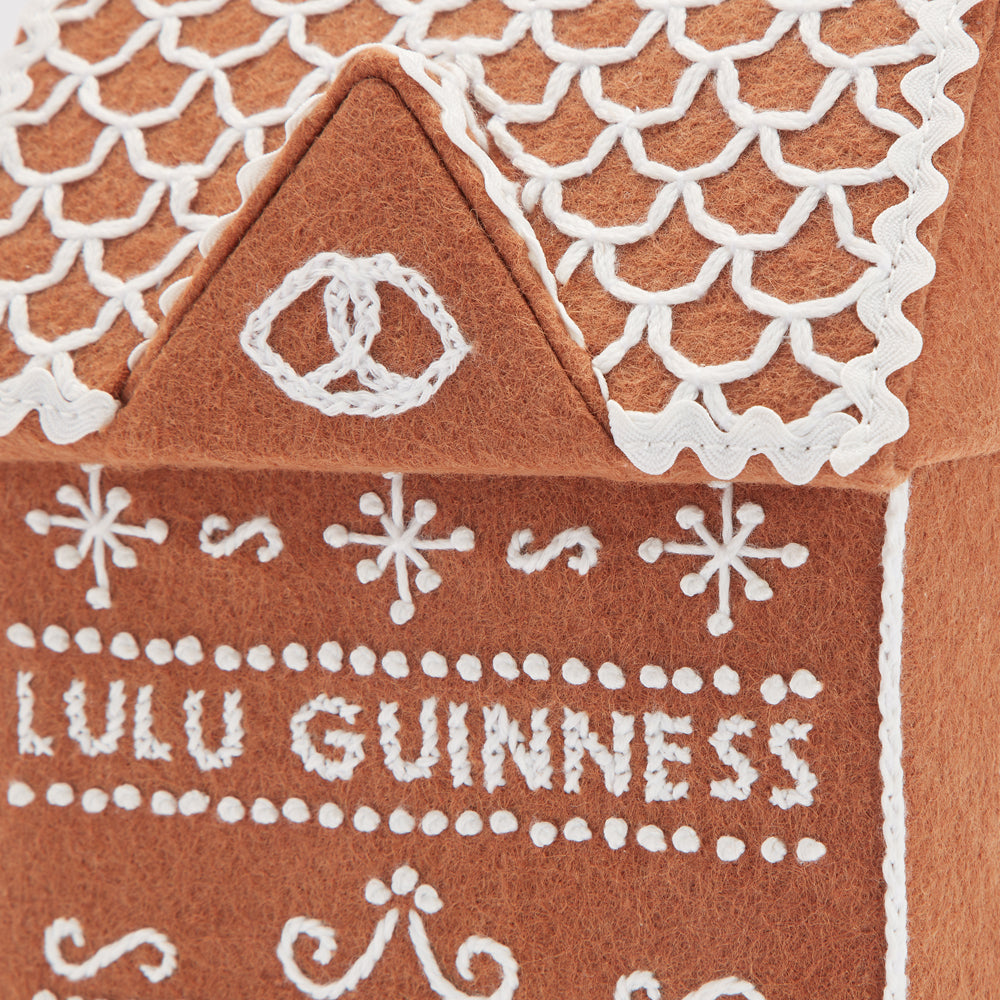 Close-up of a brown felt gingerbread house with white embroidered details, including the text "Lulu Guinness".