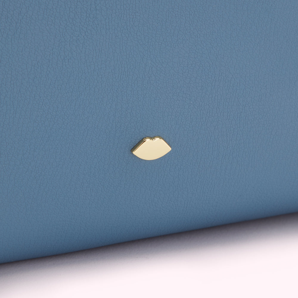 Close-up of a blue textured purse with a gold lip emblem.
