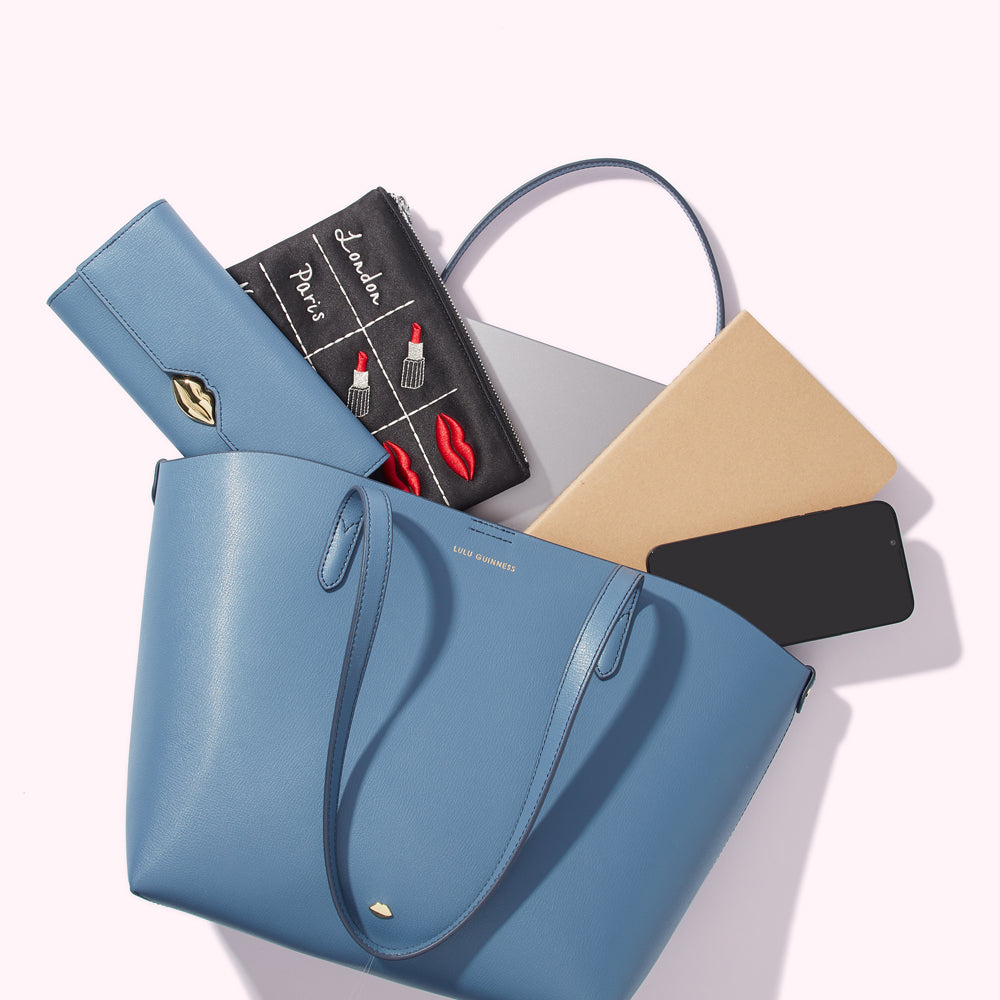 A blue tote bag overflowing with a laptop, notebook, phone, wallet, and makeup bag.