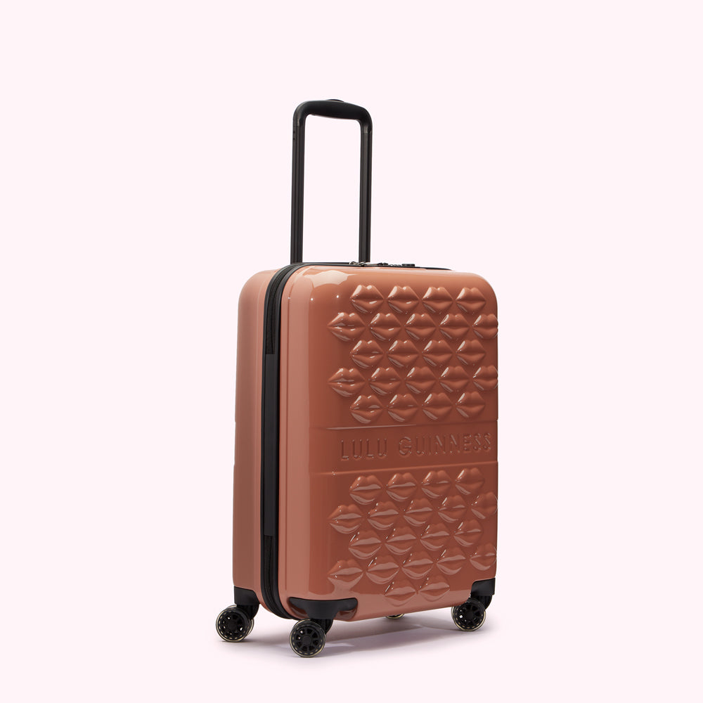 A dusty rose Lulu Guinness carry-on suitcase with a repeating lip pattern.