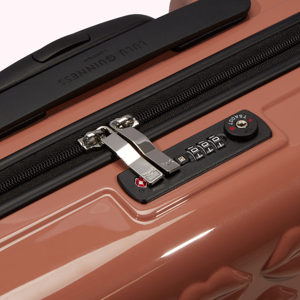 Close-up of a Lulu Guinness dusty rose pink suitcase showing the TSA-approved combination lock and zipper.
