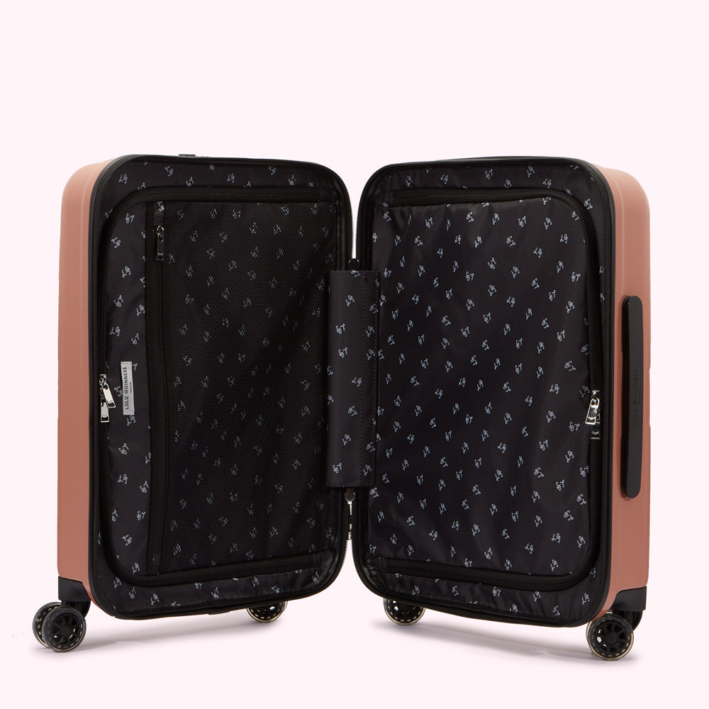 Open rose-gold Lulu Guinness suitcase with black interior showing organizational pockets and a repeating pattern.
