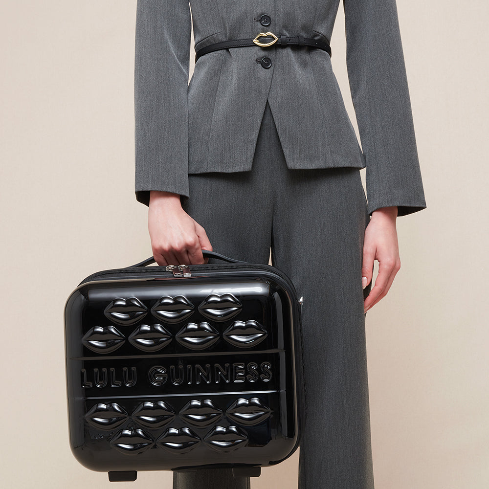 Person holding a black Lulu Guinness vanity case against a beige background