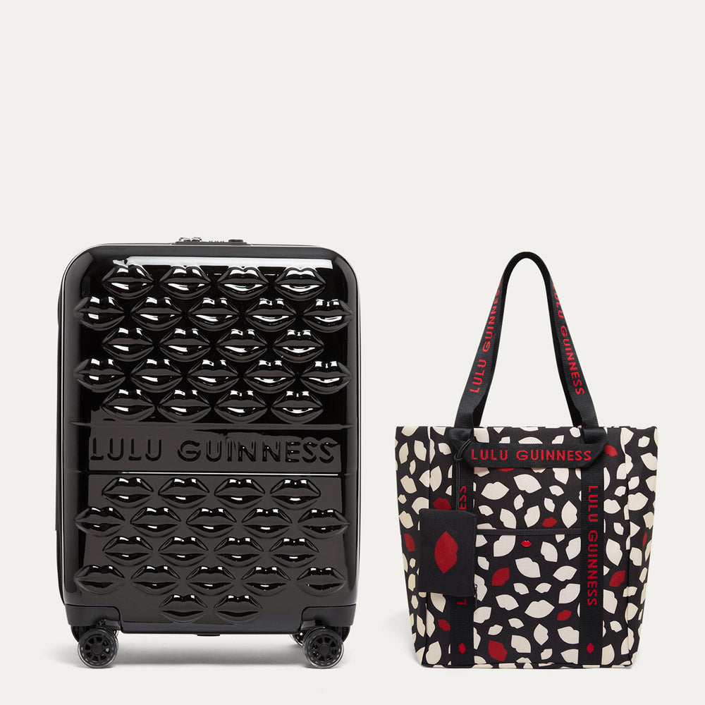 Black suitcase and patterned tote bag with Lulu Guinness branding on a light gray background
