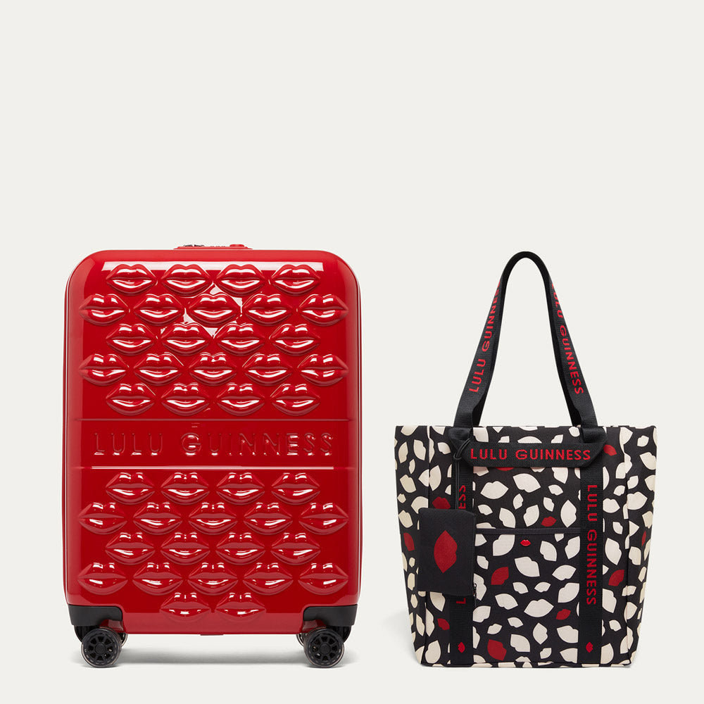 Red suitcase with lip pattern and black tote bag with lip print on a light gray background