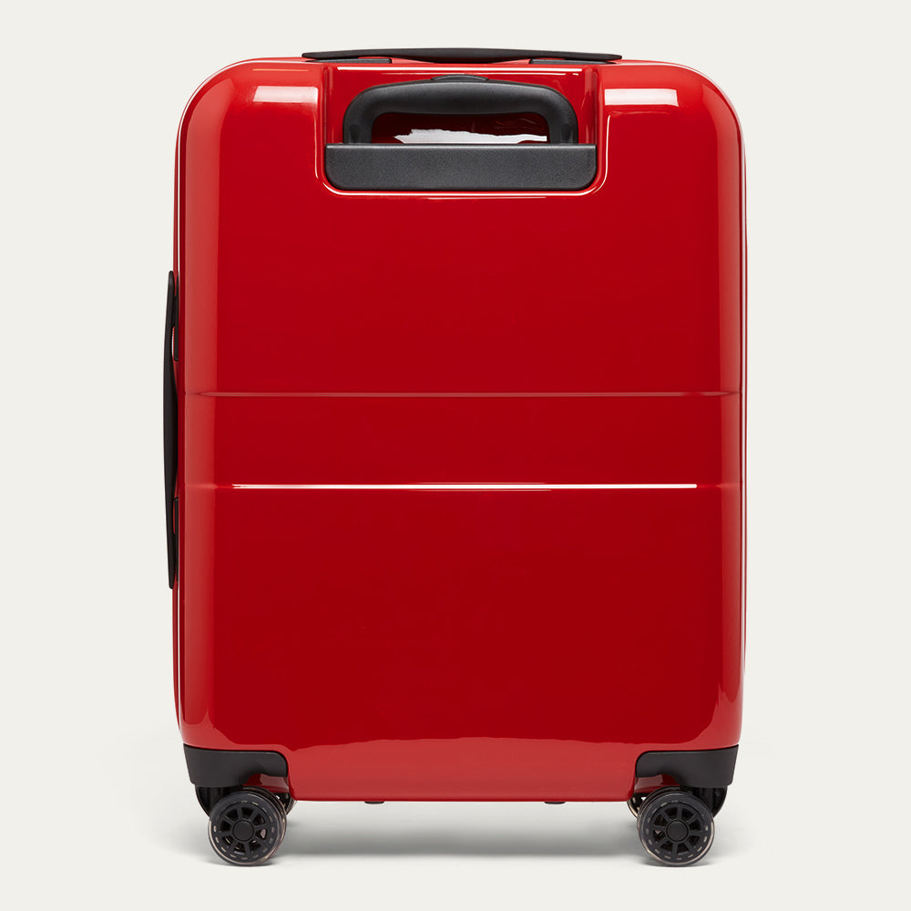 Red suitcase with black wheels and handle on a light gray background