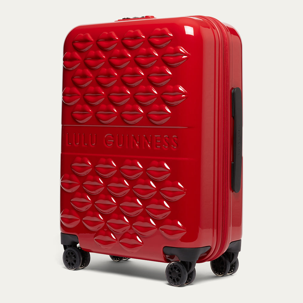 Red suitcase with a textured lip pattern and 'Lulu Guinness' branding on a light gray background