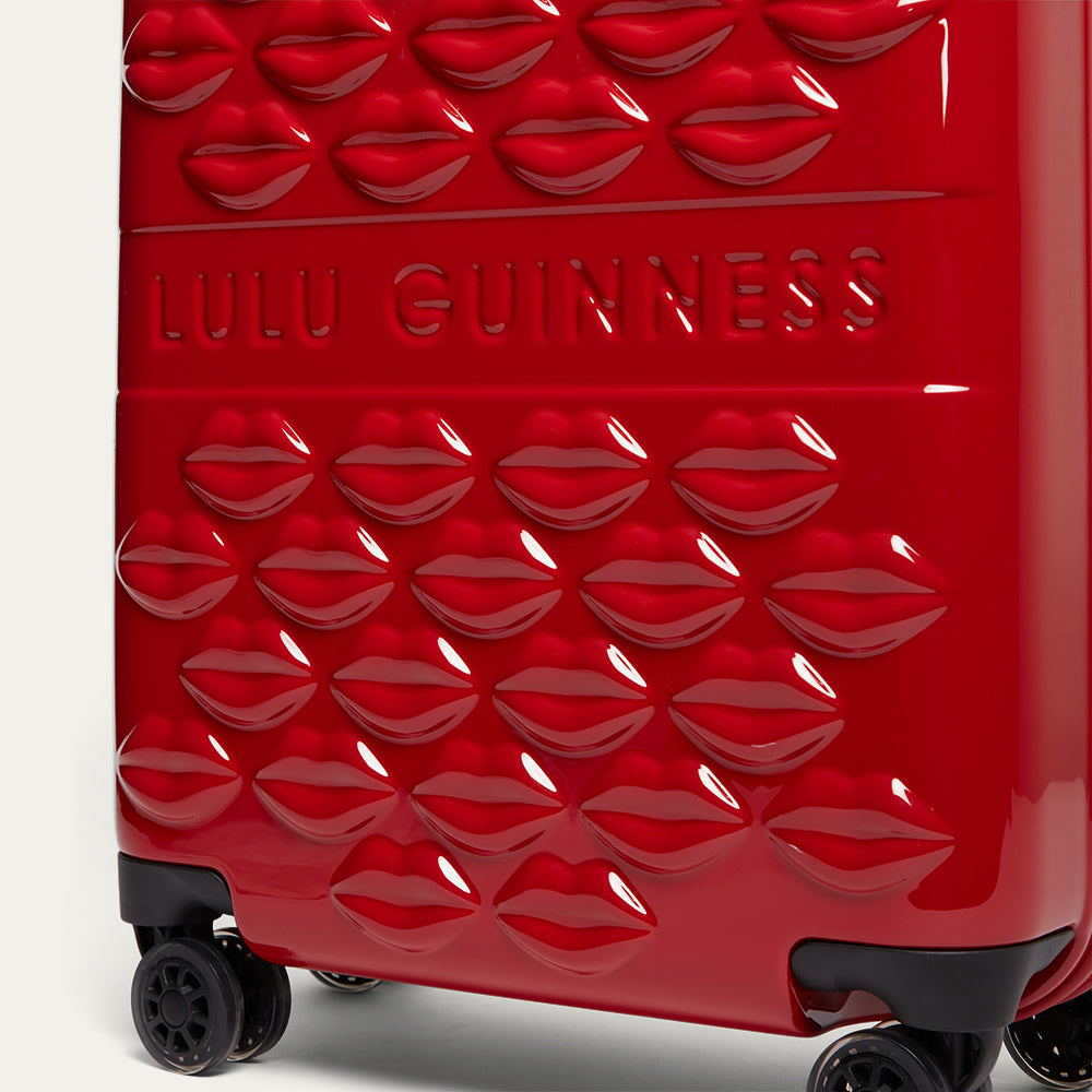 Red suitcase with lips pattern and 'Lulu Guinness' branding on a white background