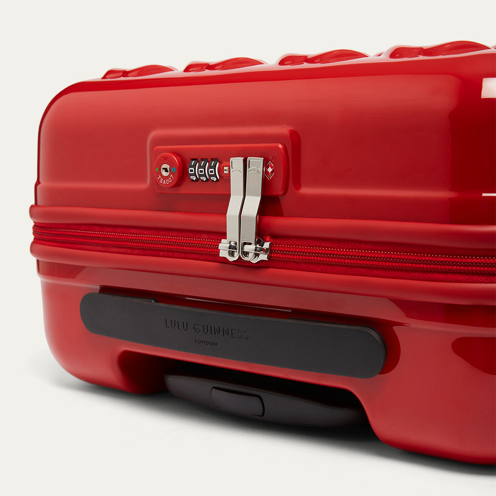 Red suitcase with a visible brand logo on a light gray background