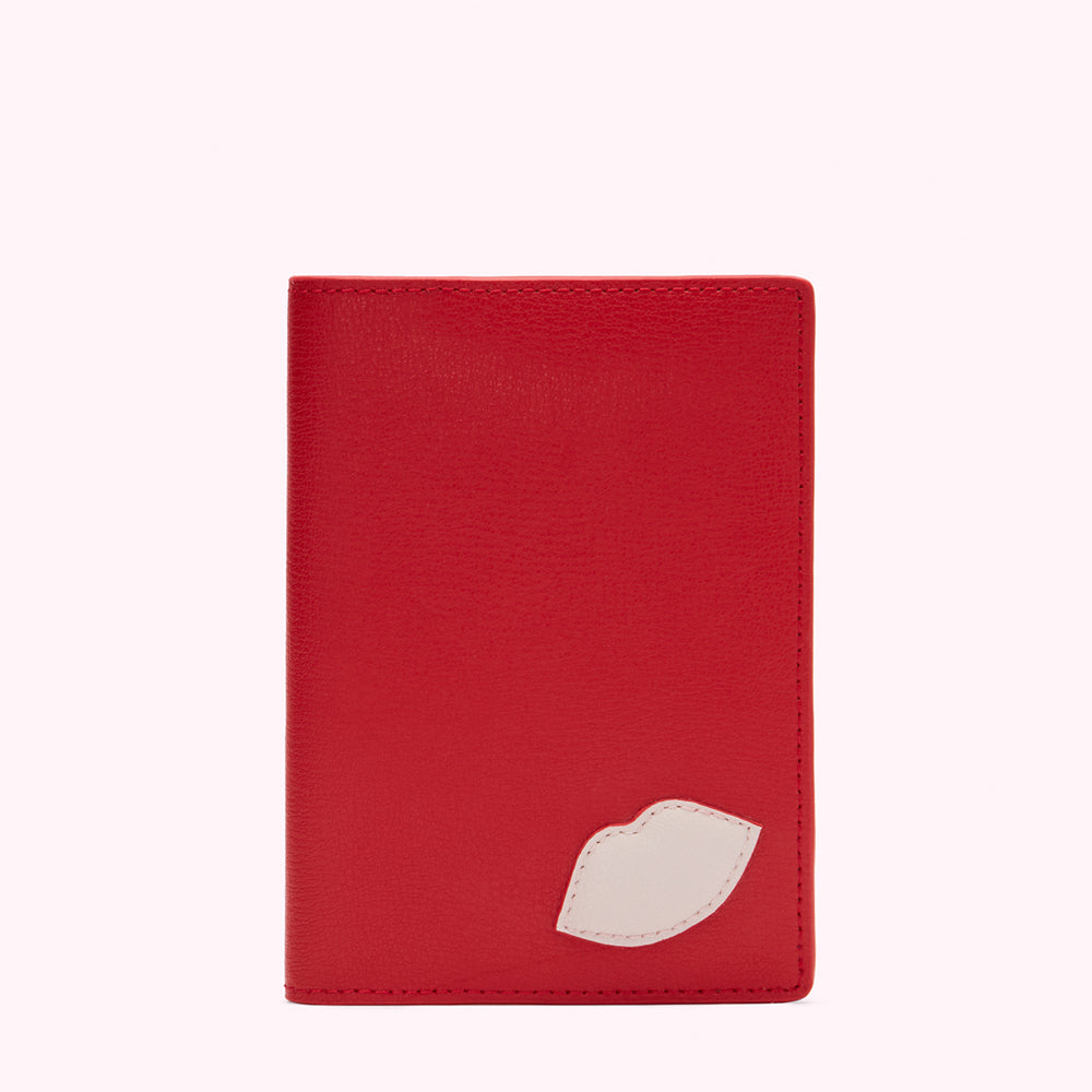 Red leather passport holder with a small off-white lip design.
