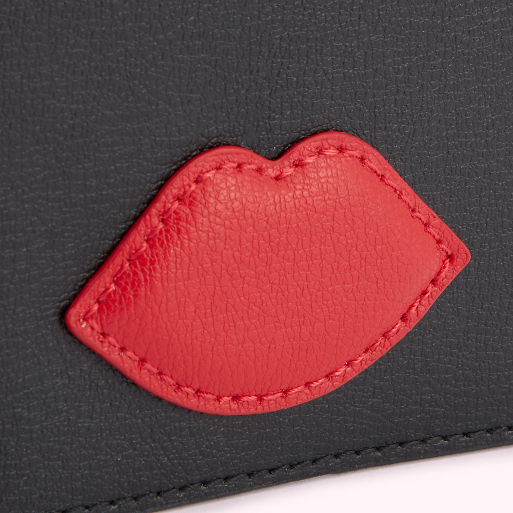 Close-up of a black leather cardholder with a red leather lip detail.
