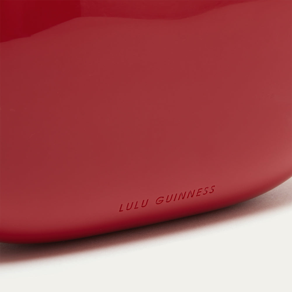 Close up image of a red clutch bag with 'Lulu Guinness' branding on a white background