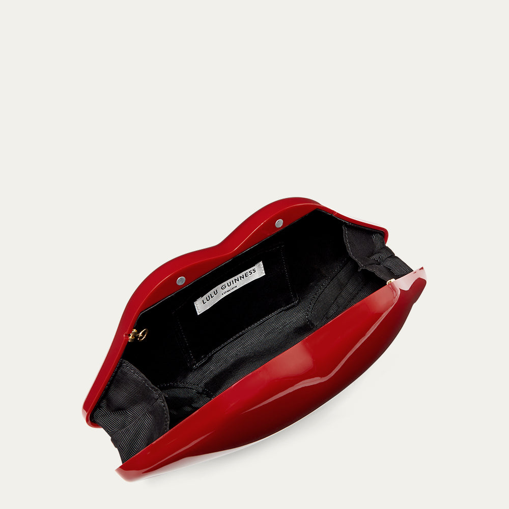 Red lip-shaped clutch bag open to reveal a black lining and a 'Lulu Guinness' branded label on a light grey background