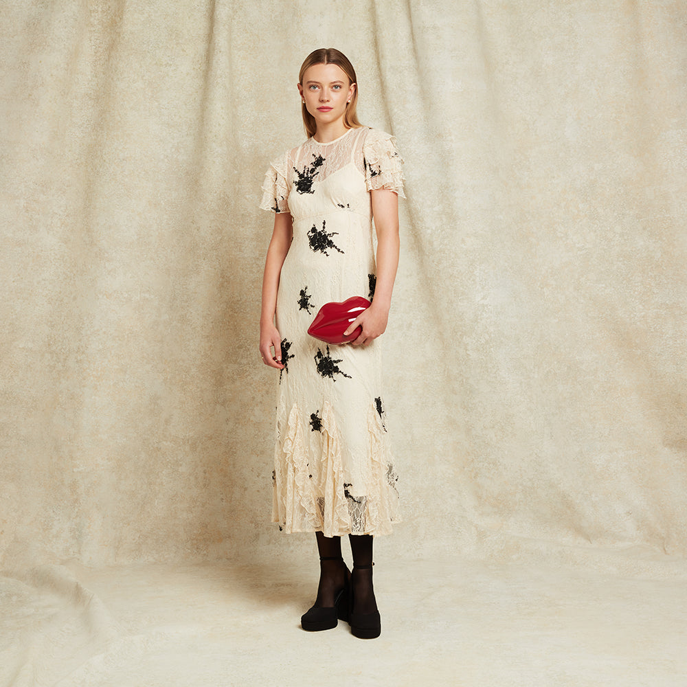 Woman wearing a floral dress holding a red lip-shaped clutch against a plain background