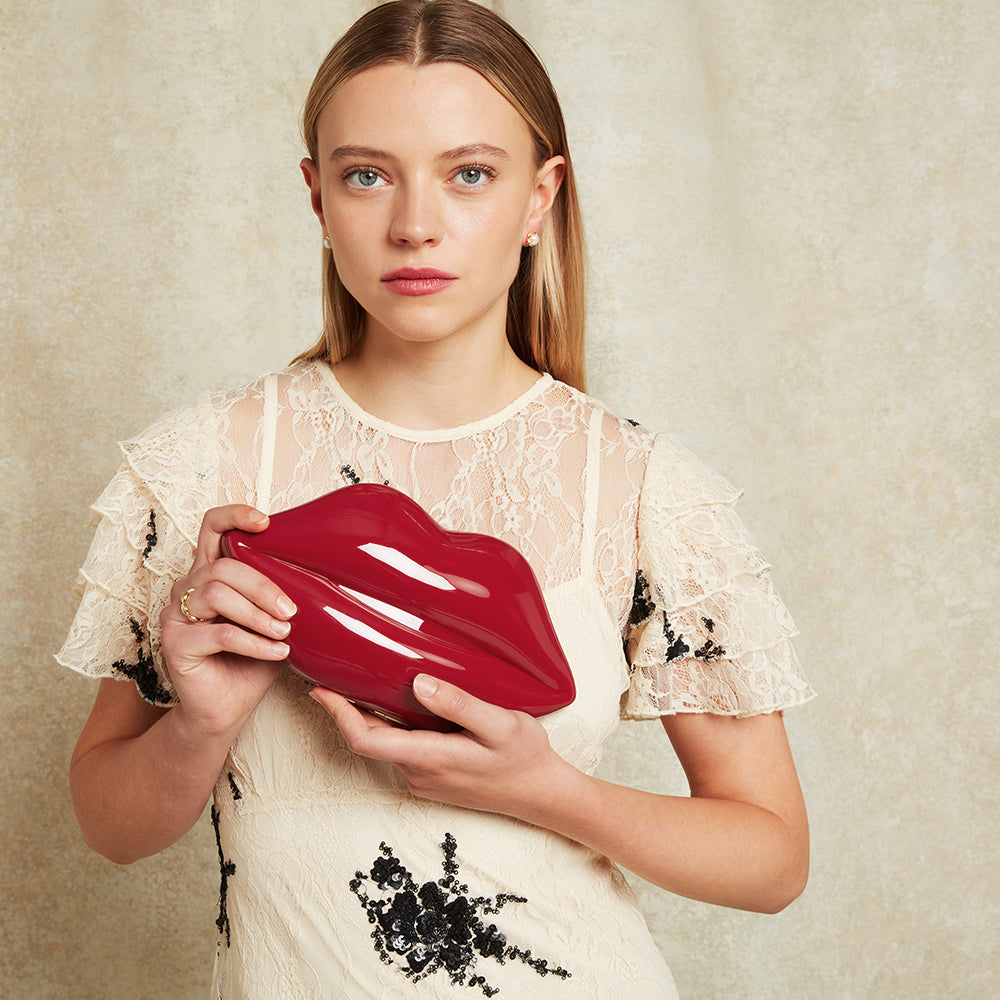 Woman holding a red lip-shaped clutch against a beige background