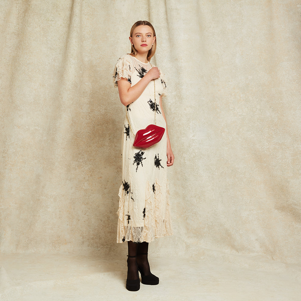 Woman wearing a floral dress with a red lip-shaped clutch bag against a plain background