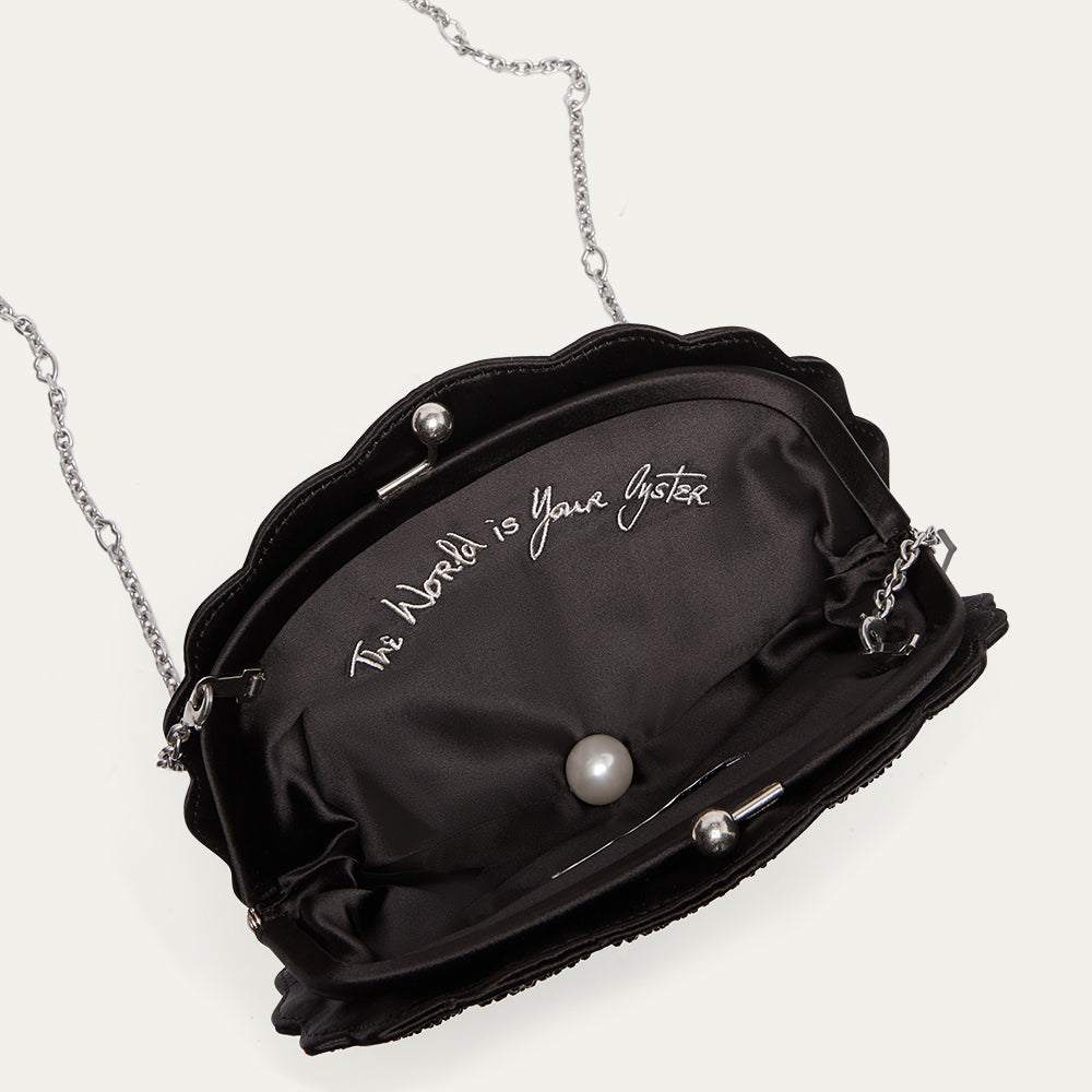 Black handbag with pearls and a chain strap on a white background