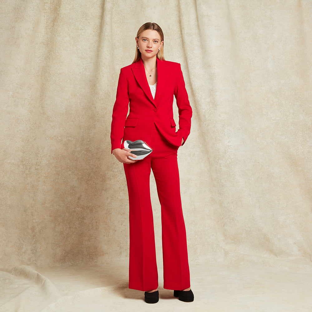 Woman in a red suit holding a silver lip-shaped clutch against a beige background