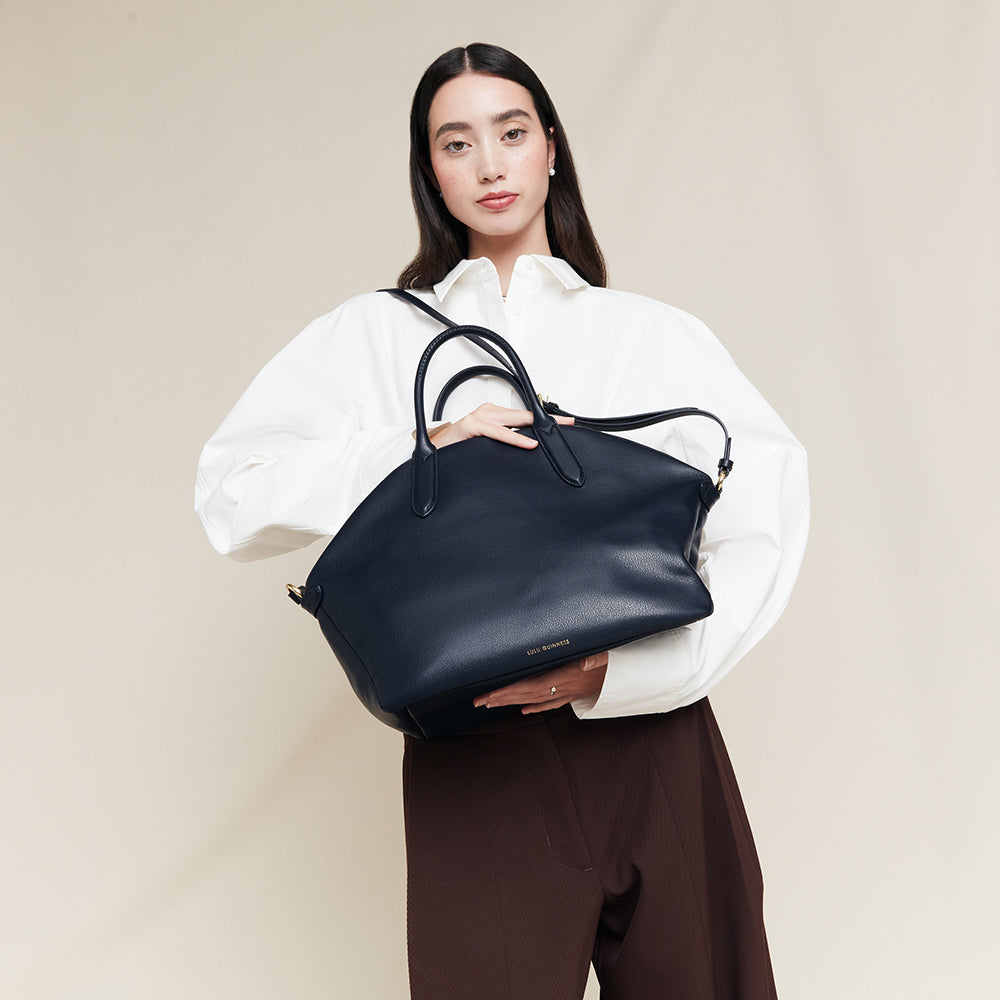 Woman holding a navy blue leather tote bag against a beige background