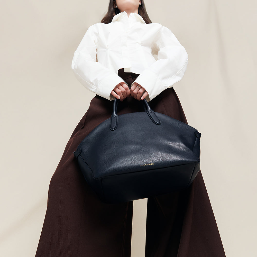 Person holding a navy blue leather tote bag against a neutral background