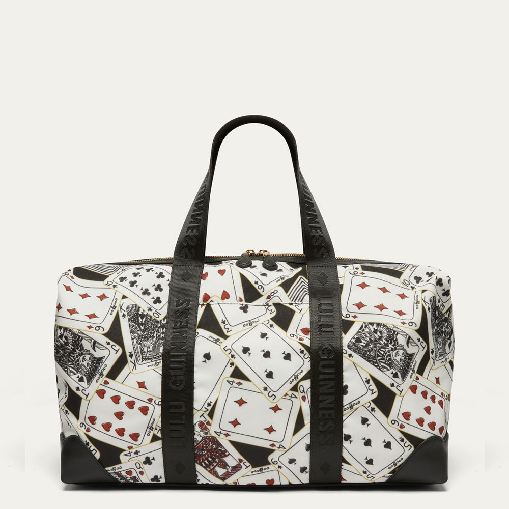 A black and white duffel bag featuring a playing card pattern with red and black suits, complete with black webbing handles and black corner protectors.