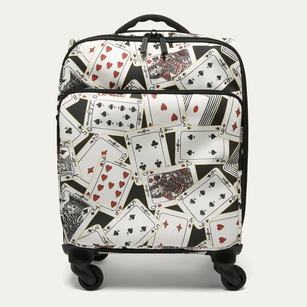 A rolling suitcase with a black, white, and red playing card pattern, featuring four spinner wheels and a top handle, shown against a light gray background.