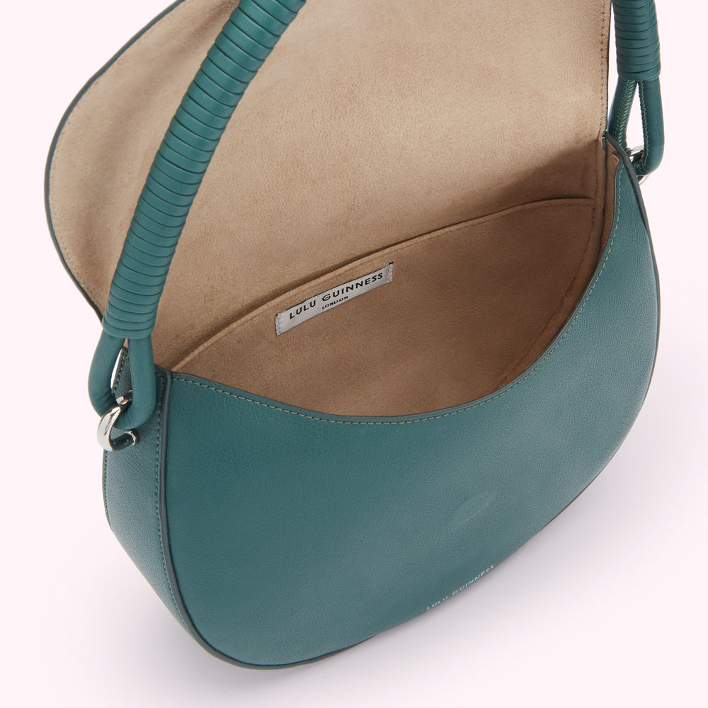 Interior view of a teal Lulu Guinness London handbag with a beige lining and a twisted teal handle.
