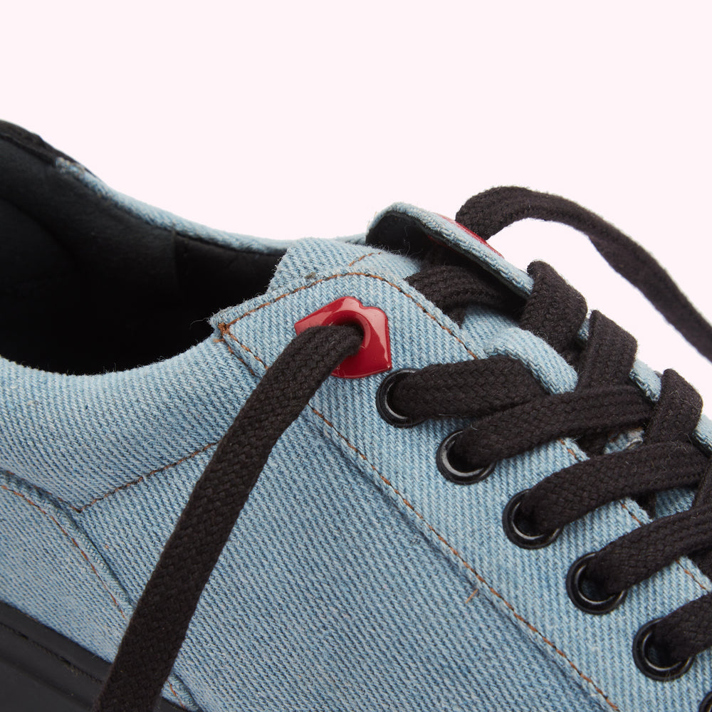 Close-up of light blue denim sneakers with black laces and red aglets.
