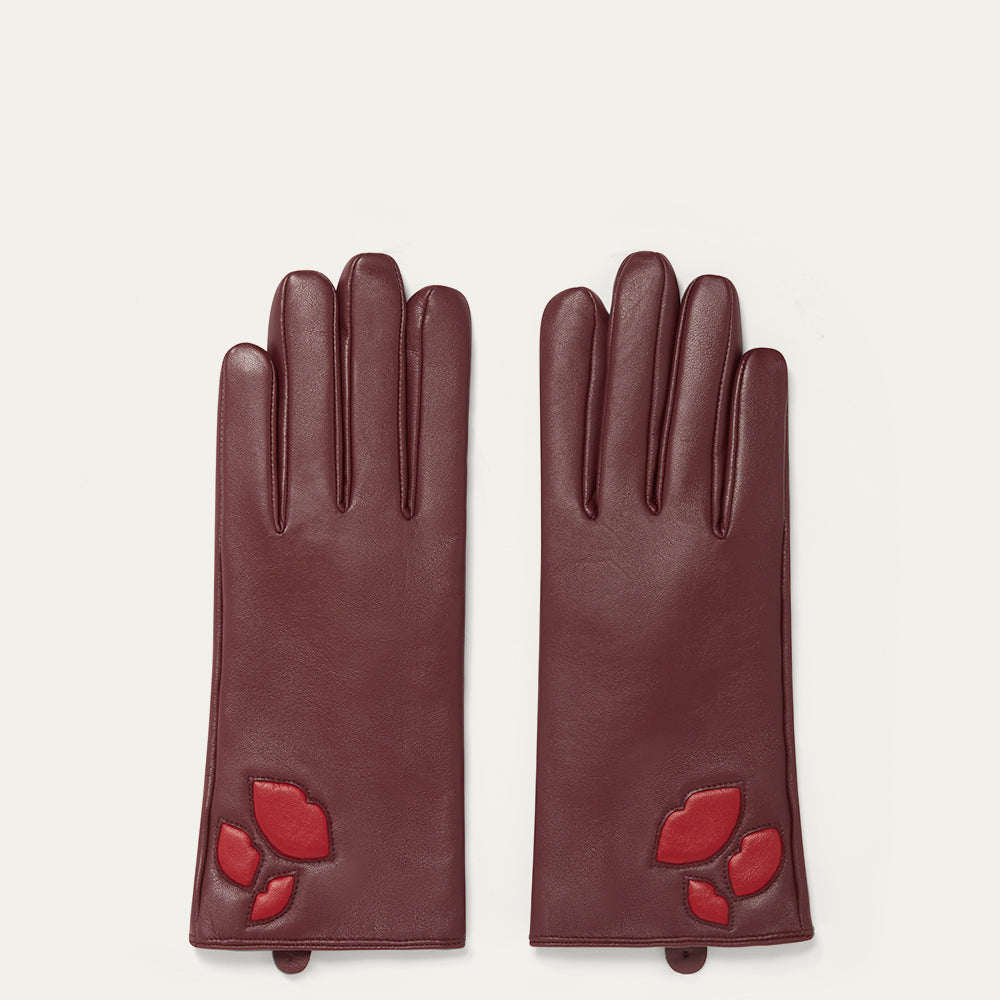 Pair of burgundy leather gloves with red lip designs on a light beige background