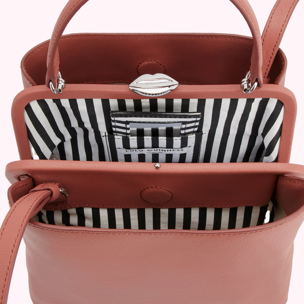 Dusty rose Lulu Guinness handbag with black and white striped interior and silver lip clasp open to reveal its interior.