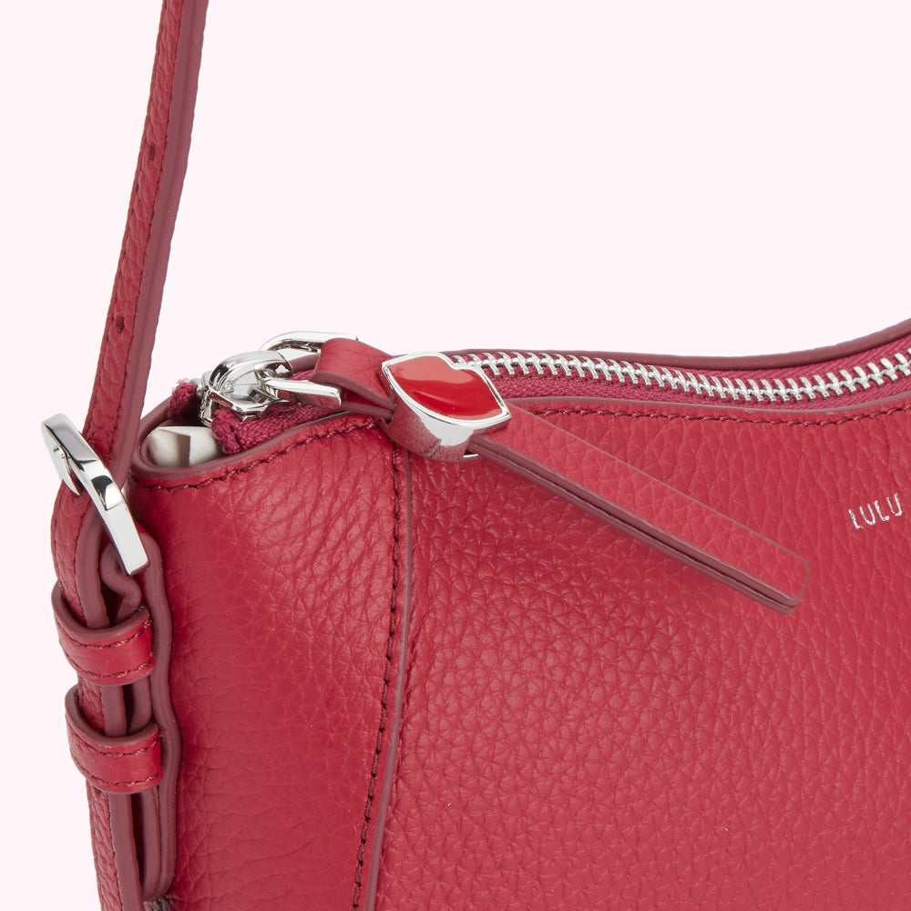 Close-up of a red Lulu Guinness leather crossbody bag with silver zipper and heart-shaped pull.
