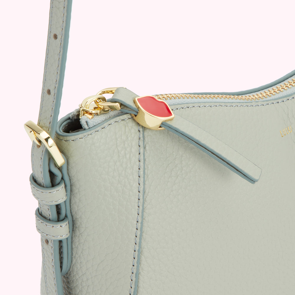 Close-up of a light blue leather crossbody bag with a gold zipper and a red and gold lip-shaped zipper pull.