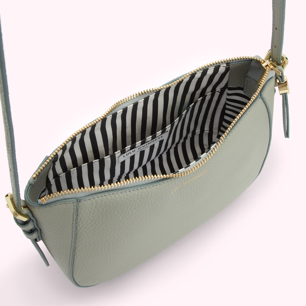 Sage green Lulu Guinness crossbody bag open to reveal its black and white striped interior.