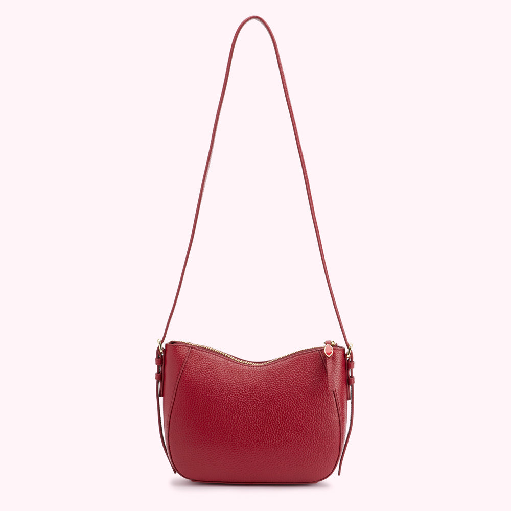 A red leather crossbody bag with a curved shape and gold zipper.
