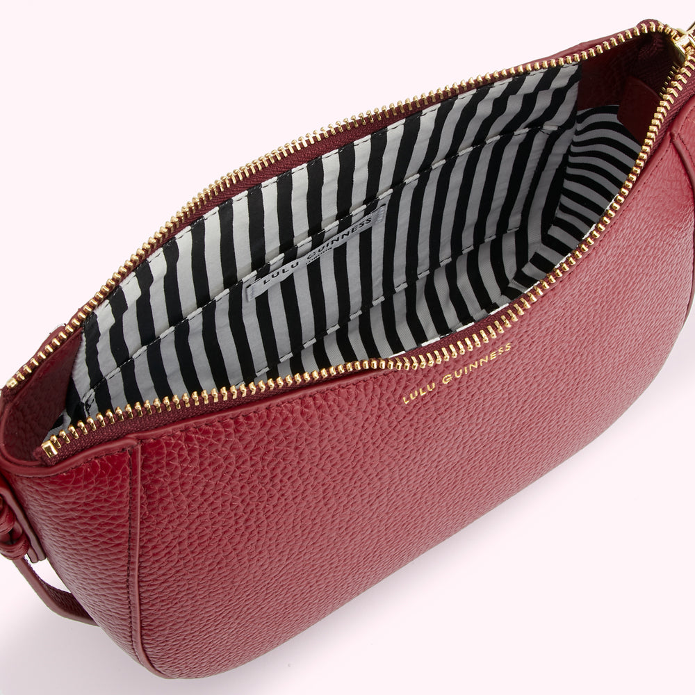 Open red Lulu Guinness crossbody bag with black and white striped interior.

