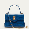 A blue croc-effect embossed leather handbag with a top handle, gold-tone clasp, and a gold chain strap, shown against a plain light background.