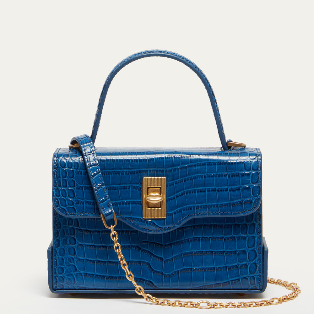 A blue croc-effect embossed leather handbag with a top handle, gold-tone clasp, and a gold chain strap, shown against a plain light background.