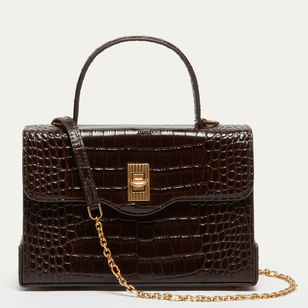 A dark brown croc-effect embossed leather handbag with a top handle, a gold-tone turn-lock clasp, and a gold chain shoulder strap, shown against a plain off-white background.