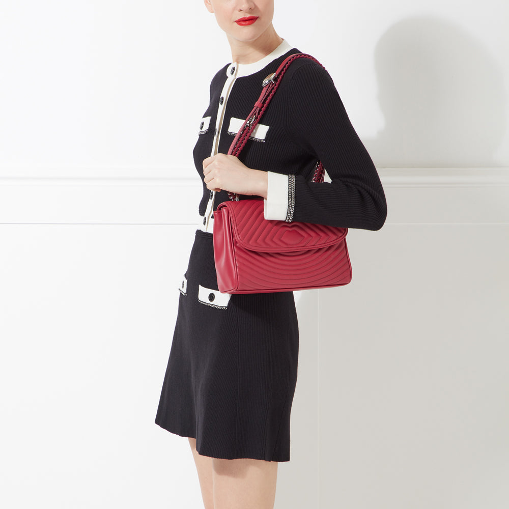 Woman in black and white dress holding a red quilted shoulder bag.
