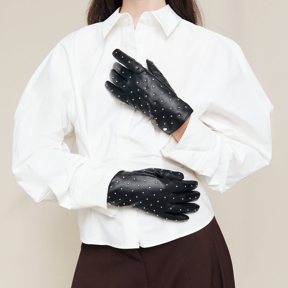 Person wearing black leather studded gloves and a white shirt on a beige background