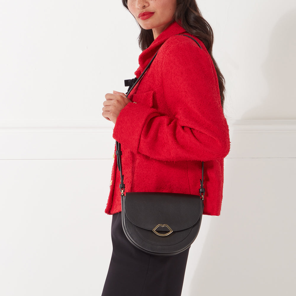 Woman in red jacket holding black half-moon crossbody bag with gold lip detail.

