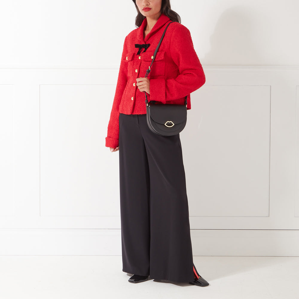 Woman in red jacket and black pants wearing a black purse with gold lip detail.
