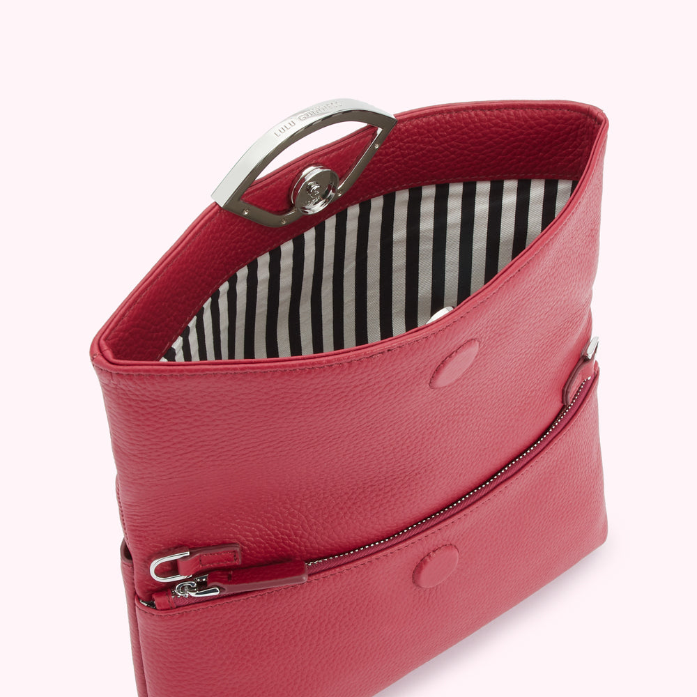 Red Lulu Guinness crossbody bag open to reveal its black and white striped interior.
